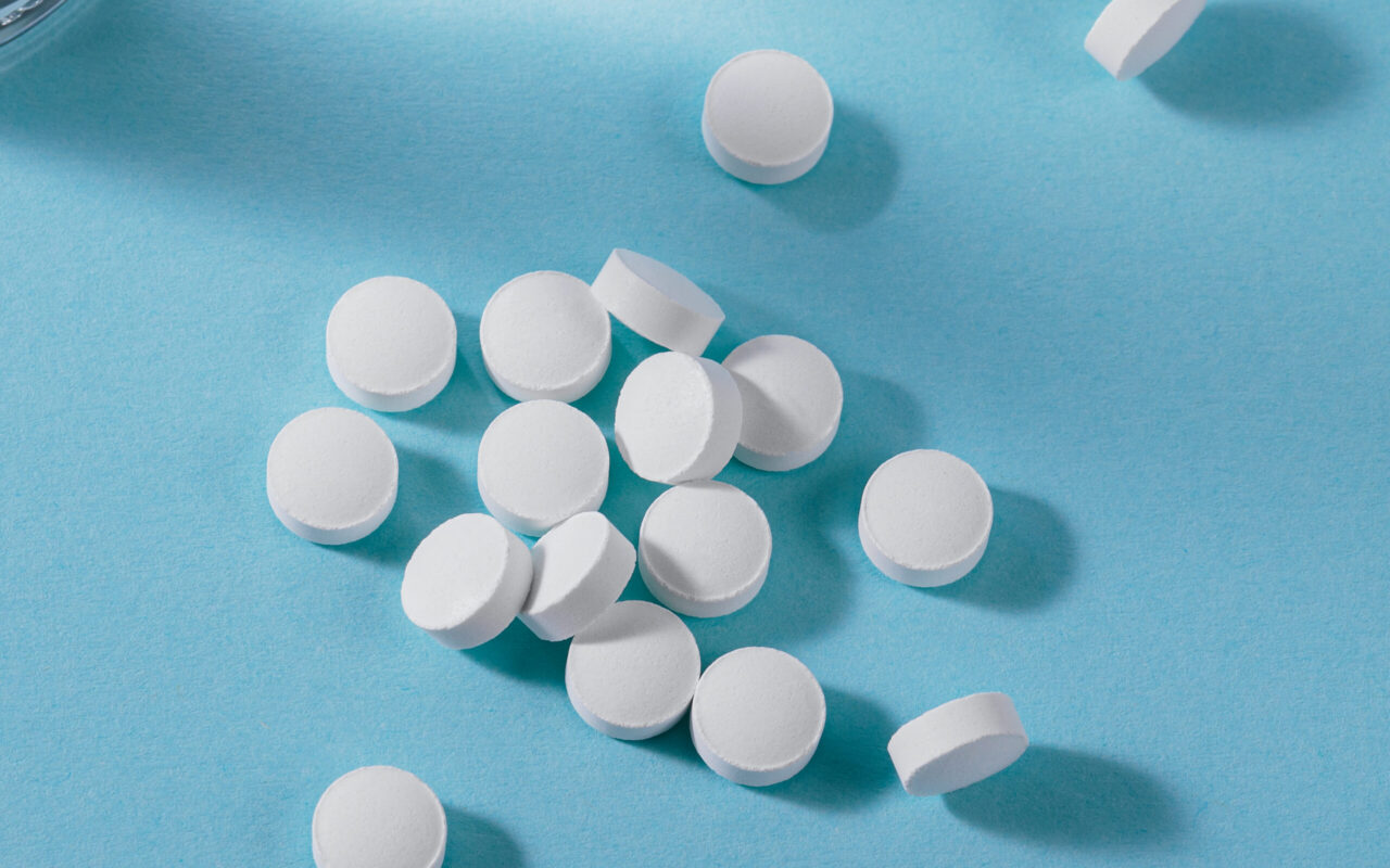 Herbal and Vitamin white pills healthy food freely laid near glass of water on light blue background for healthy eating in daily life